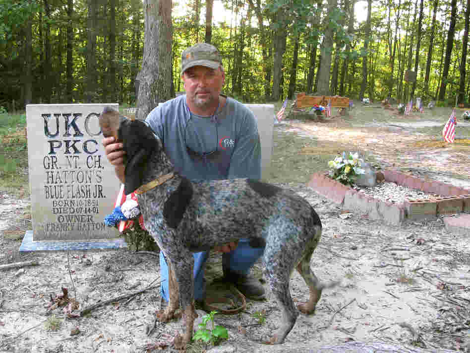 Franky Hatton and Cletis pose in front of the gravestones of Hatton's champion coon hounds at Coon Dog Cemetery.