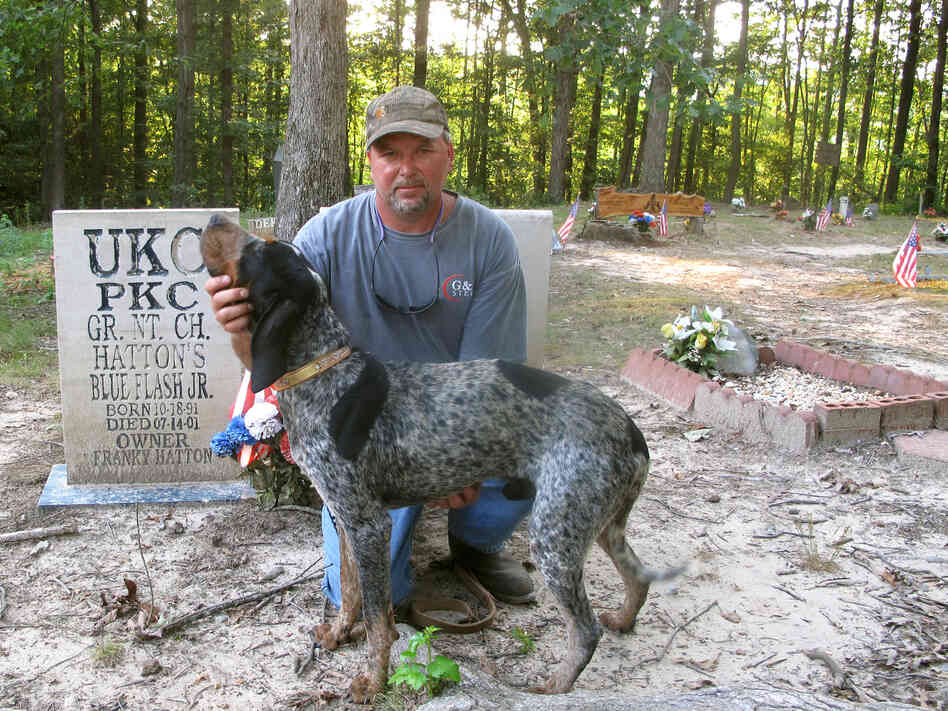 Franky Hatton and Cletis pose in front of the gravestones of Hatton's champion coon hounds at Coon Dog Cemetery.