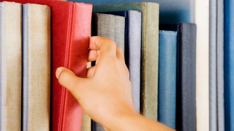 Image of a hand selecting a red book from a bookshelf