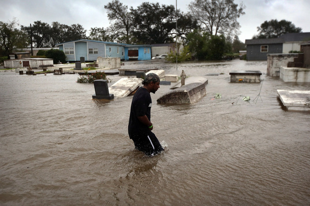 Errol Ragas walks past a cemetery to recover dry blankets from his home as rising waters from Hurricane Isaac flood the neighborhood  of Oakville in Plaquemines Parish, Louisiana.