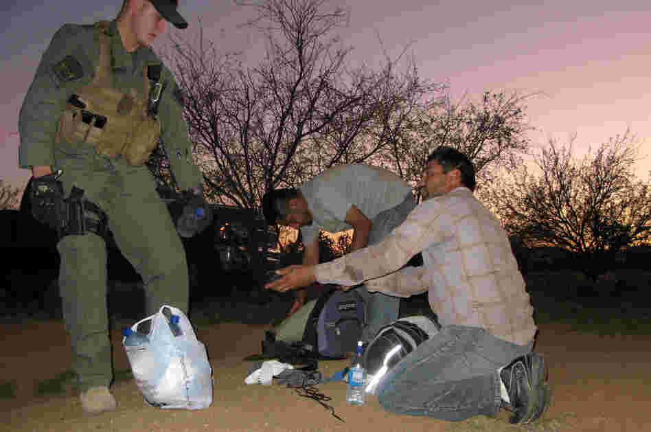 A Border Patrol agent offers water to two men caught after illegally entering the U.S. through the Arizona desert. Roughly 80,000 federal workers have jobs related to immigration enforcement.