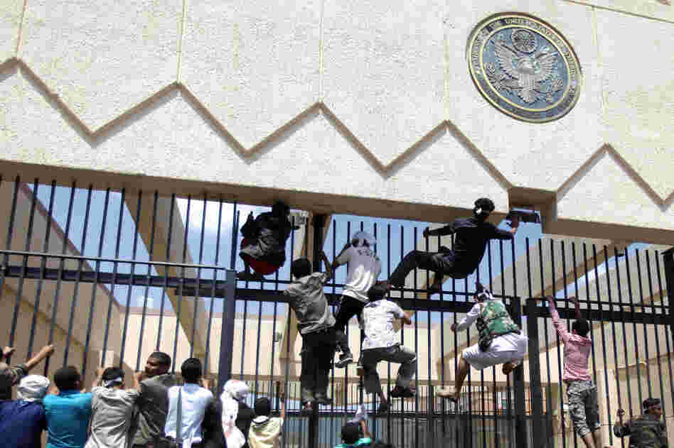 Protesters climb a fence at the embassy as security guards fire warning shots into the air.