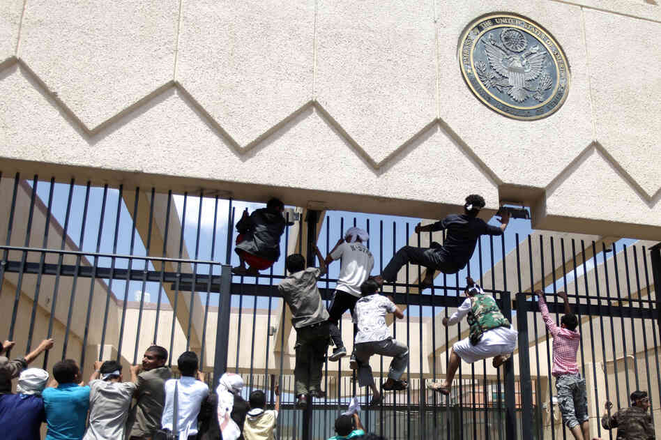 Protesters climb a fence at the embassy as security guards fire warning shots into the air.