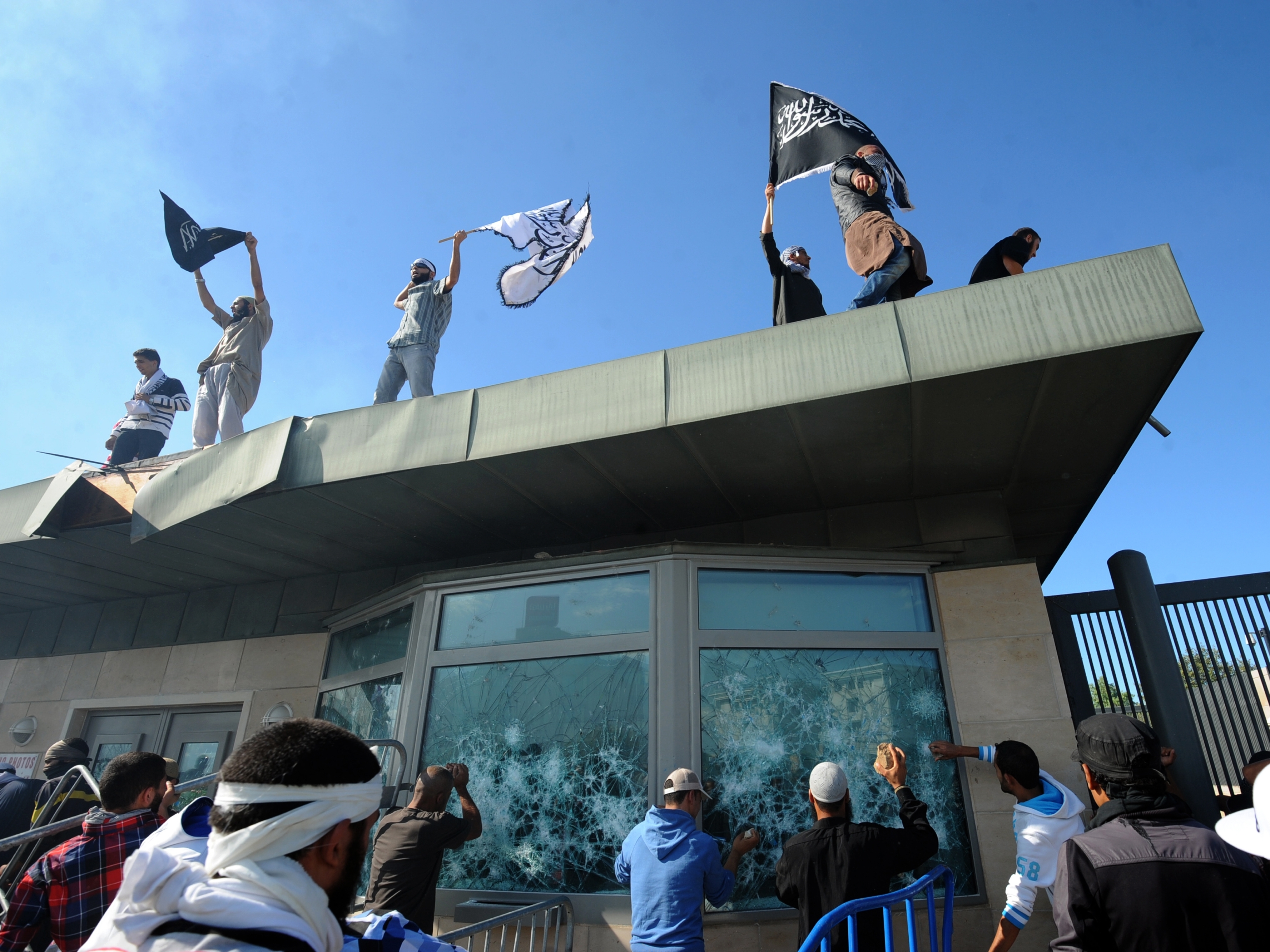 Tunisian protesters break the windows as they hold Islamic flags above the gate of US embassy in Tunis during a protest against a film mocking Islam on September 14, 2012.