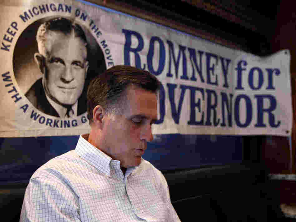 Mitt Romney reads on his campaign bus earlier this year. A 1960s campaign poster supporting his father, George, is behind him.