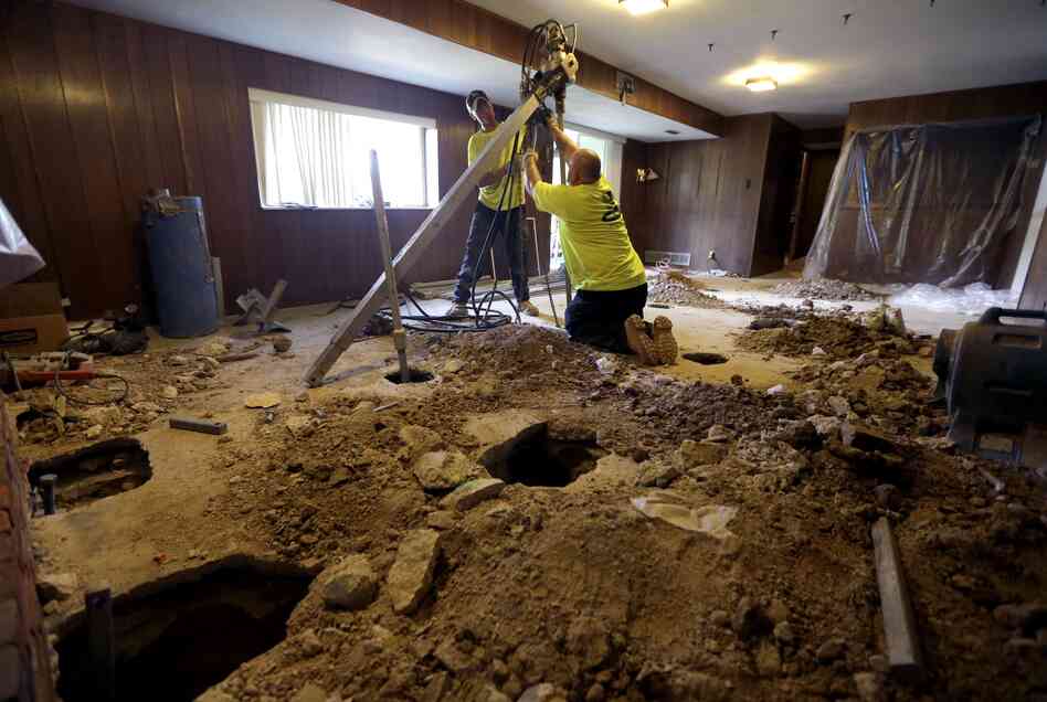 Contractors drive piers into the ground to stabilize a settling home in Manchester, Mo. on Aug. 29, 2012.