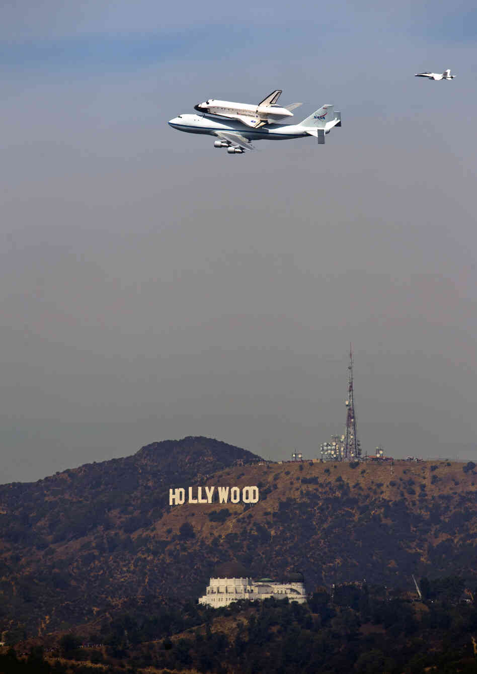 The Space Shuttle Endeavour passes the Hollywood Sign and the Griffith Observatory as seen from Dodger Stadium Friday.