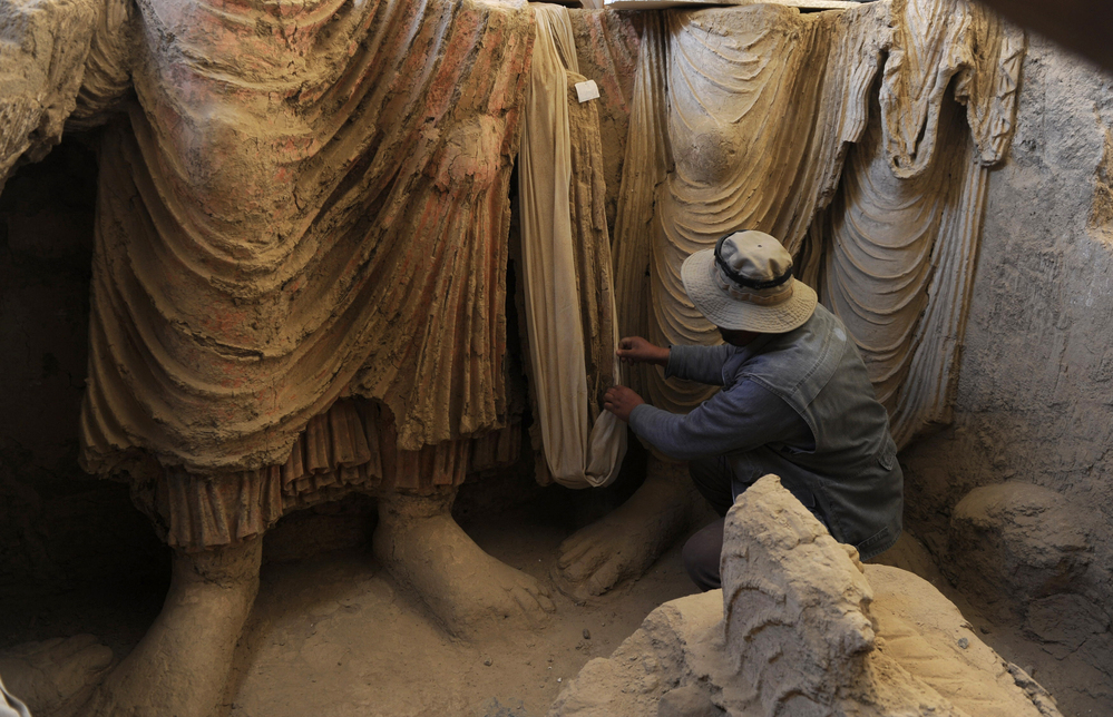Above, an Afghan archaeologist drapes a fabric across the remains of Buddha statues discovered inside an ancient monastery in Mes Aynak on Nov. 23, 2010.