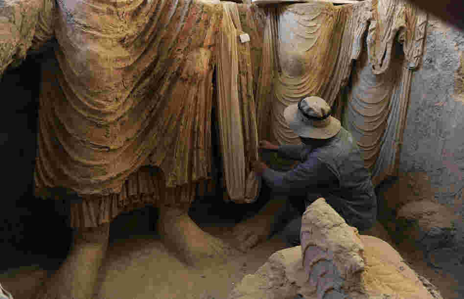 Above, an Afghan archaeologist drapes a fabric across the remains of Buddha statues discovered inside an ancient monastery in Mes Aynak on Nov. 23, 2010.