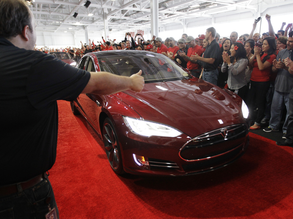 Tesla workers cheer on one of the first Tesla Model S cars sold, during a rally at the Tesla factory in Fremont, Calif., in June. The company is now unveiling a new network of refueling stations for the vehicles.