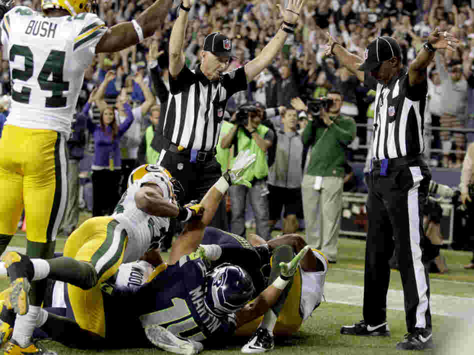 Confusion: One official (to the  left) signals touchdown for Seattle. The other signals that a touchback — possession — for Green Bay.