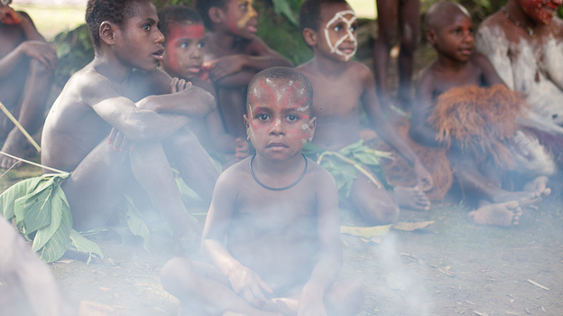 A boy sits next to cooking fire at a Papua New Guinea village. Many villages re-create traditional dress and customs to cater to tourists and their search for an "authentic" experience.