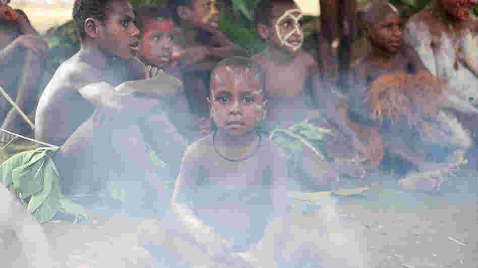 A boy sits next to cooking fire at a Papua New Guinea village. Many villages re-create traditional dress and customs to cater to tourists and their search for an "authentic" experience.