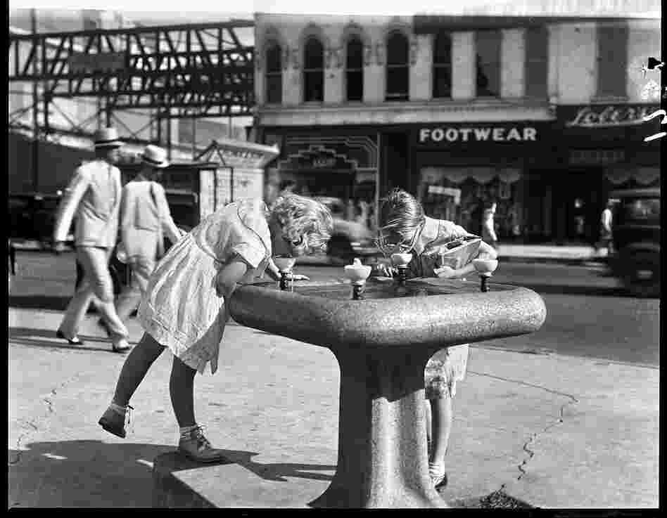 Girls drink from a water fountain on the courthouse square, circa 1930.