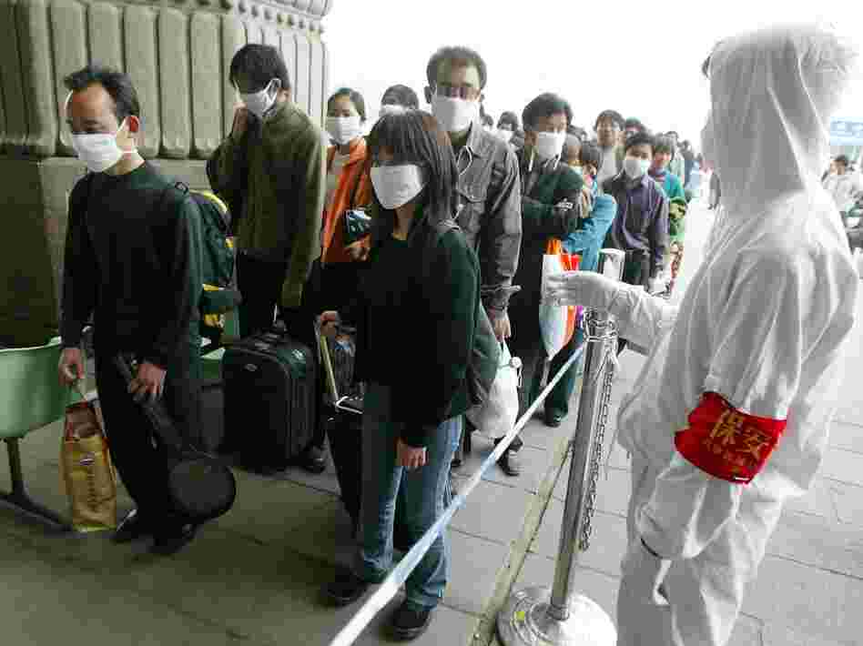 A railway worker wearing protective clothing to ward off the SARS virus controls a line of travelers as they wait to enter Beijing's West Railway Station Tuesday in 2003.