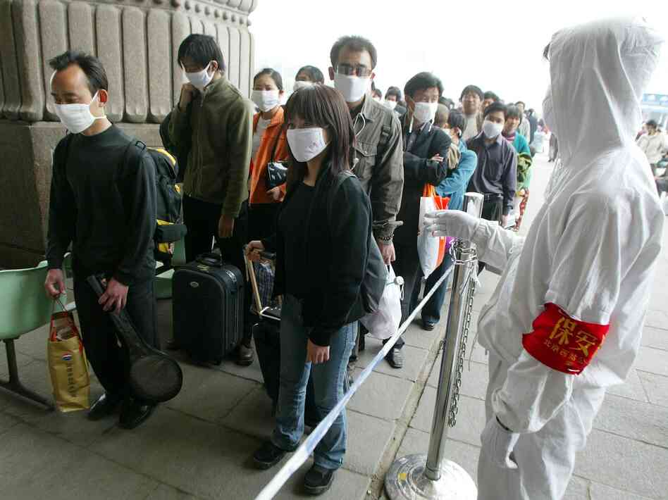 A railway worker wearing protective clothing to ward off the SARS virus controls a line of travelers as they wait to enter Beijing's West Railway Station Tuesday in 2003.