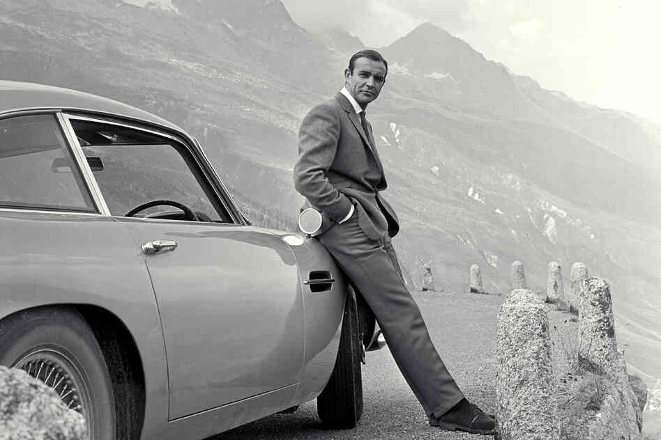 Sean Connery relaxes on the bumper of his Aston Martin DB5 during the filming of location scenes for Goldfinger in the Swiss Alps in 1964.