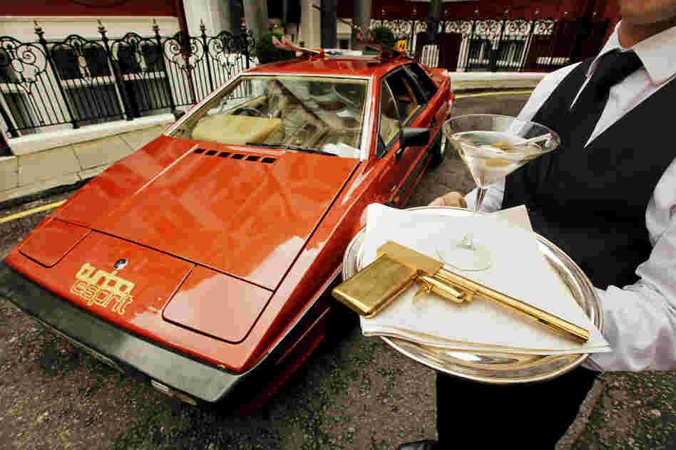 A model holds a limited-edition gold-plated Golden Gun replica, near a Lotus Turbo Esprit car from 1981's For Your Eyes Only.