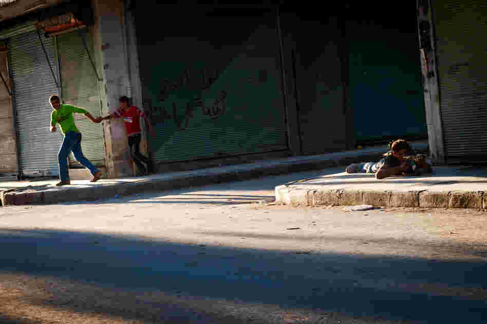 Young Syrians run for cover as a Free Syrian Army fighter returns sniper fire in the Bustan Pasha neighborhood of Aleppo, Aug. 21.