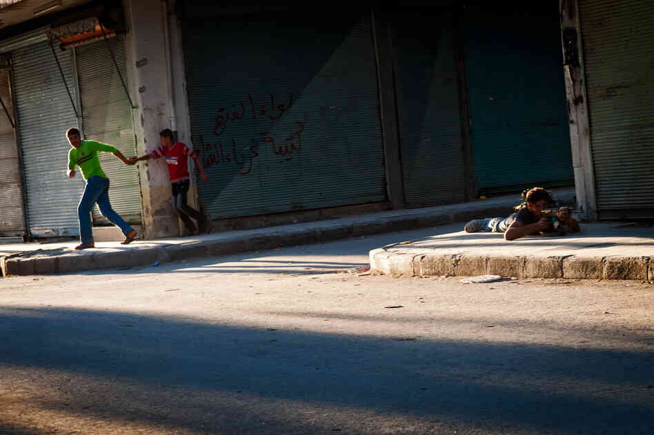 Young Syrians run for cover as a Free Syrian Army fighter returns sniper fire in the Bustan Pasha neighborhood of Aleppo, Aug. 21.