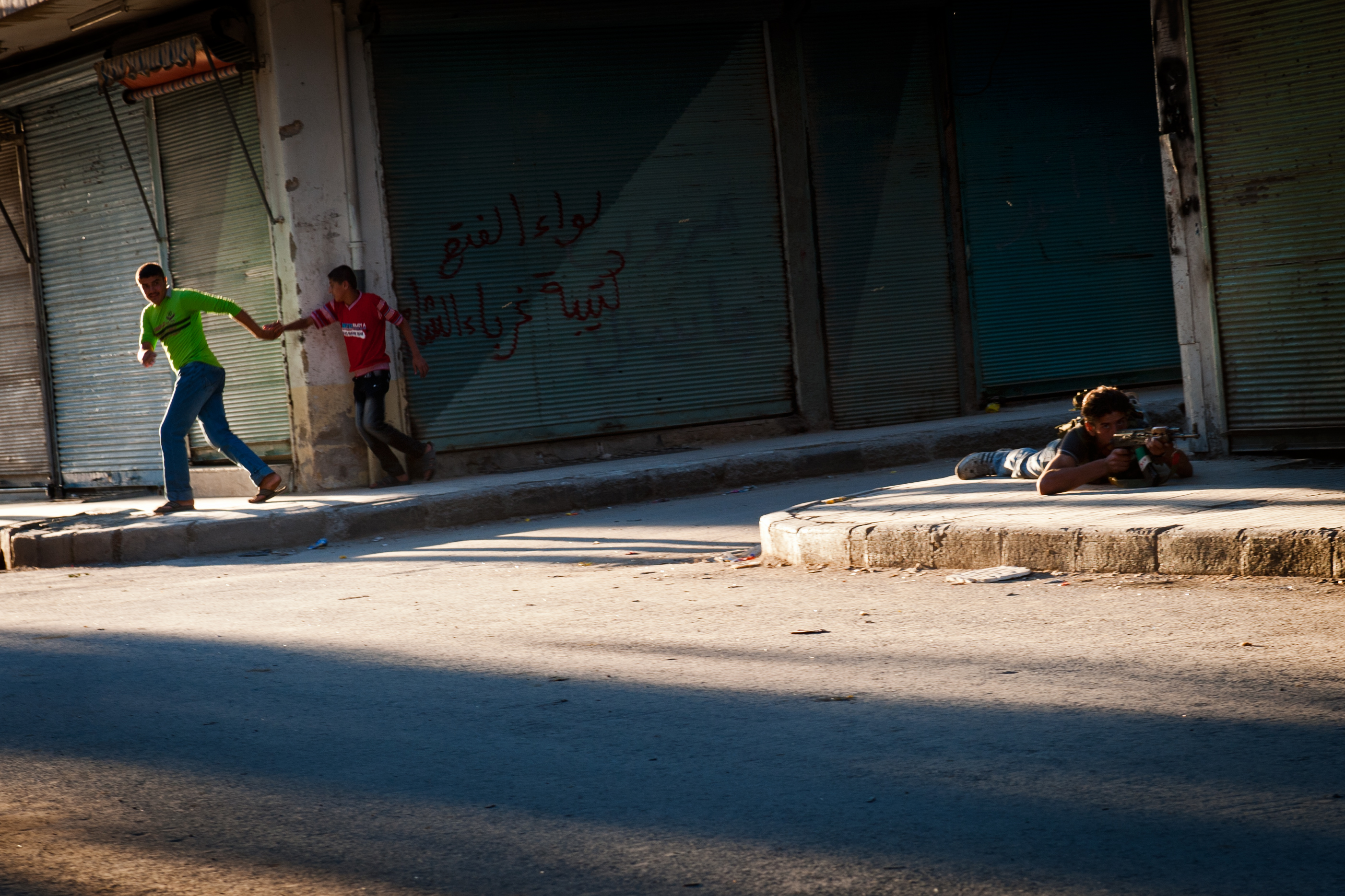 Young Syrians run for cover as a Free Syrian Army fighter returns sniper fire in the Bustan Pasha neighborhood of Aleppo, Aug. 21.