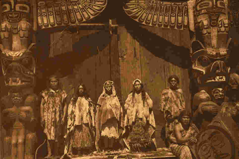 The original caption reads: "The [Kwakiutl] bride stands in the middle between two dancers hired for the occasion. Her father is at the left, and the bridegroom's father at the right behind a man who presides over the box-drum."