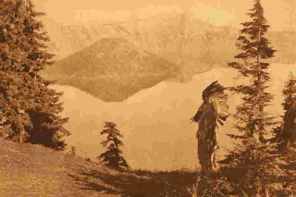 For a photo simply titled "Chief — Klamath," the caption reads: "The subject of this plate, in deerskin suit and feathered war-bonnet of the Plains culture, is shown against a background of Crater lake and its precipitous rim towering a thousand feet above the water."