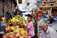 A boy chooses fruit from a stall as Jerusalem market vendors swirl around him.
