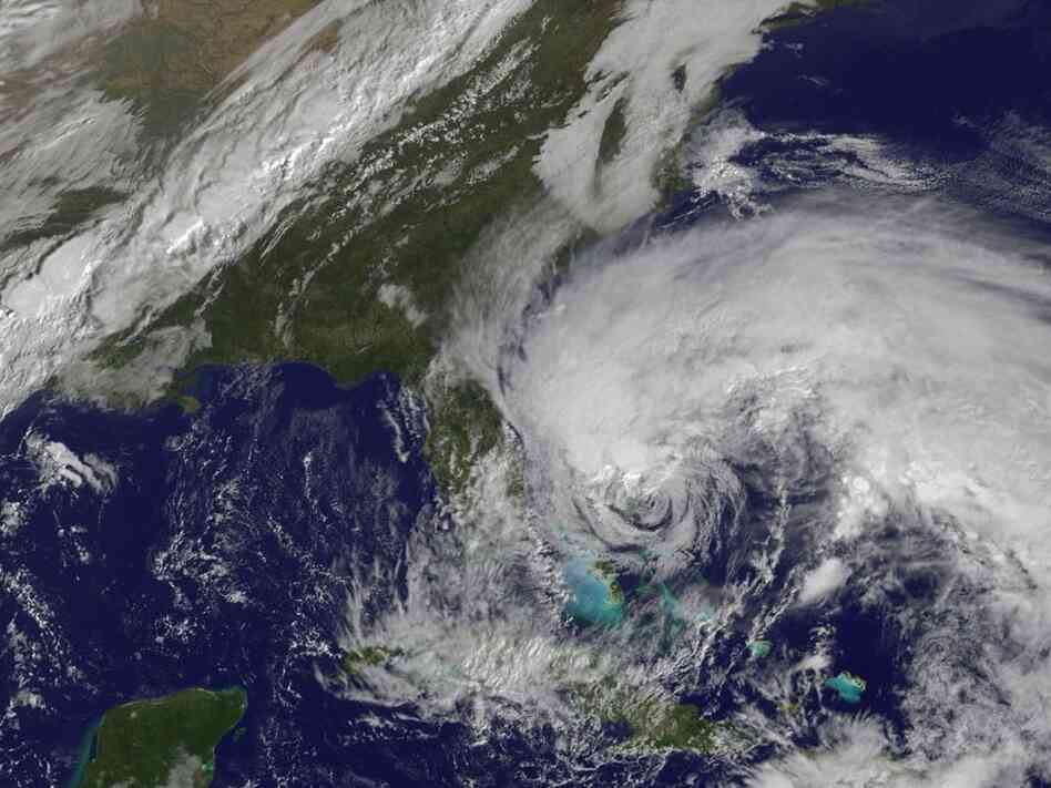 In this satellite image provided Friday by the National Oceanic and Atmospheric Administration, Hurricane Sandy's huge cloud extent of up to 2,000 miles churns over the Bahamas, as a line of clouds associated with a powerful cold front approaches the East Coast of the U.S.