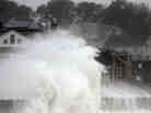 Waves crash over a road as Hurricane Sandy comes up the coast Monday in Winthrop, Mass. Economists are predicting the storm will cost tens of billions of dollars.