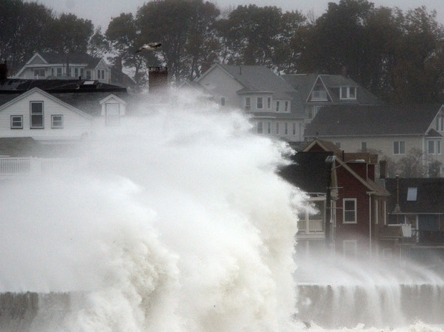 Waves crash over a road as Hurricane Sandy comes up the coast Monday in Winthrop, Mass. Economists are predicting the storm will cost tens of billions of dollars.