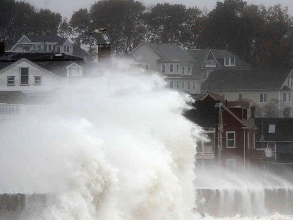 Waves crash over a road as Hurricane Sandy comes up the coast Monday in Winthrop, Mass. Economists are predicting the storm will cost tens of billions of dollars.