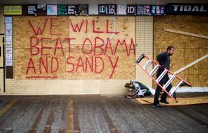 Raymond Souza carries away a ladder after boarding up a gift shop on the boardwalk in Rehoboth Beach, Del. President Obama and Gov. Romney have cancelled campaign events on Monday in anticipation of the superstorm.