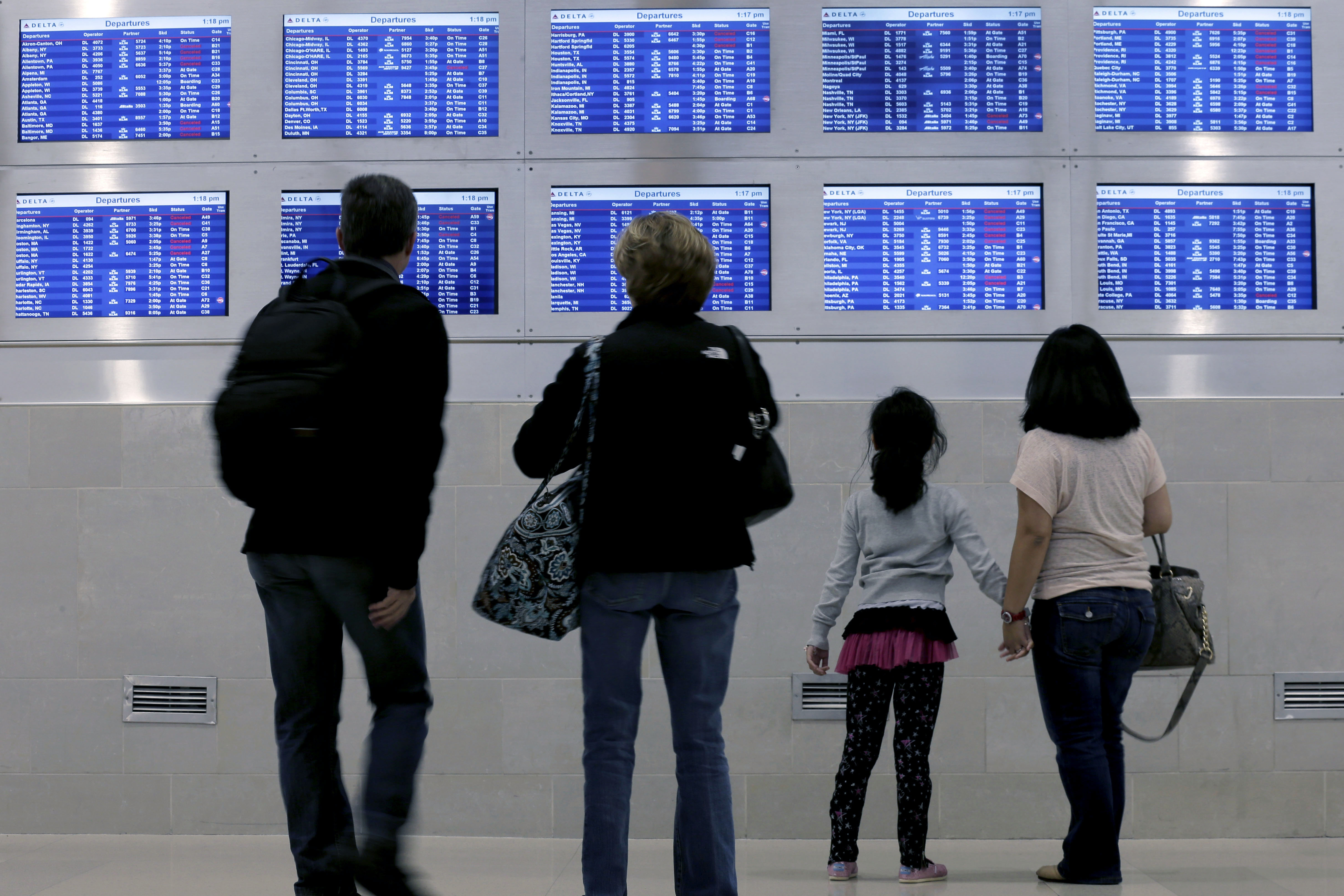 Travelers on Delta Airlines look at a departure screen in Detroit as dozens of departing flights have been canceled.