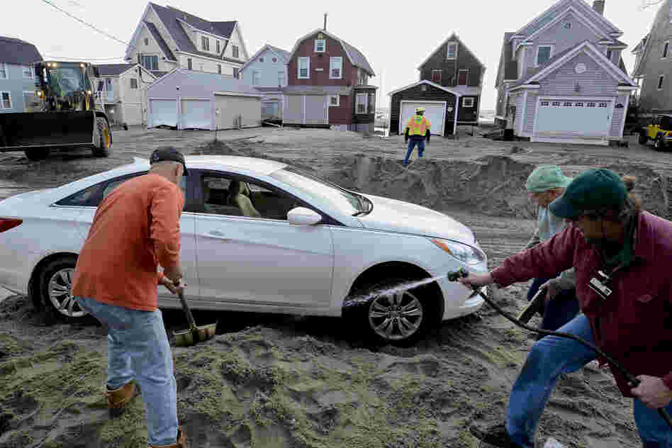 People work to free a car stuck in beach sand deposited during high tide in Milford, Conn.