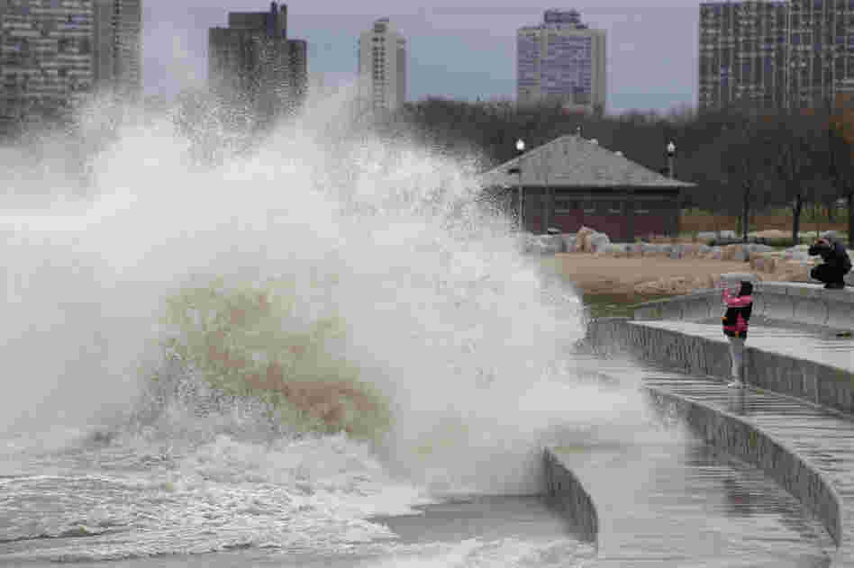 Onlookers take photos as strong waves created by Sandy crash against the Lake Michigan waterfront on the South Side of Chicago, Ill.