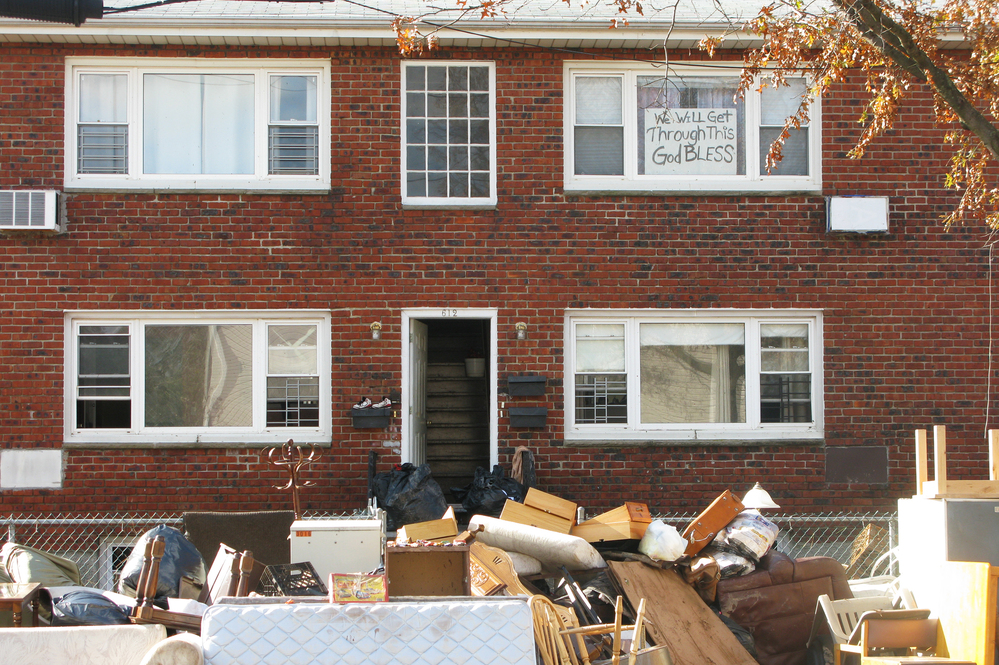 An apartment building's contents are placed on sidewalk in an effort to clean up after Sandy. The sign in the window reads, "We will get through this. God bless."