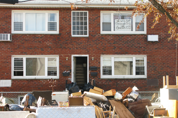 An apartment building's contents are placed on the sidewalk during cleanup from Superstorm Sandy. The sign in the window reads, "We will get through this. God bless."