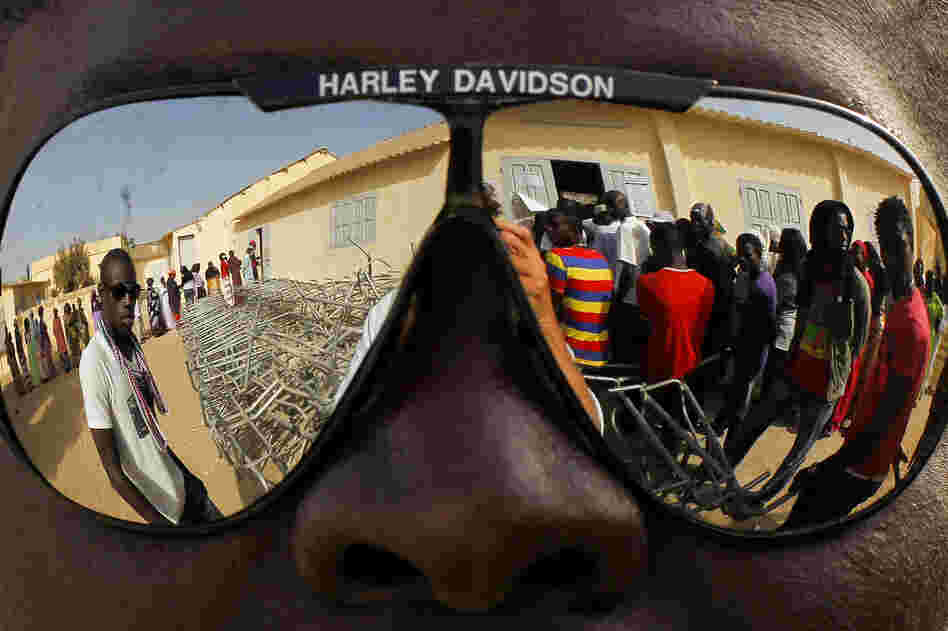 Voters in Senegal, reflected in a pair of sunglasses, wait to cast ballots in the presidential election in Senegal, 2012.
