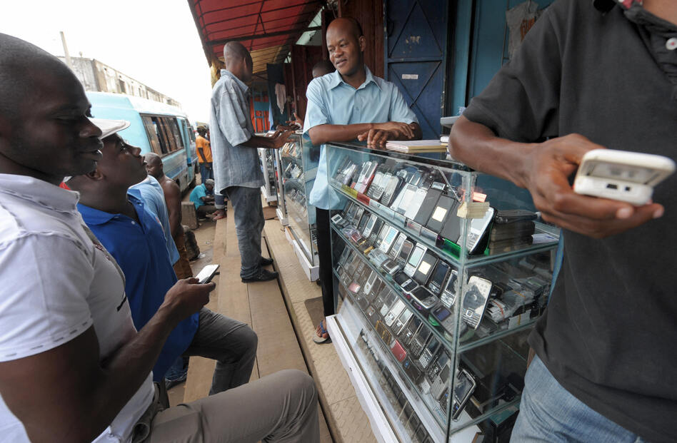 Men look at mobile phones at the Adjame market in Abidjan, Ivory Coast. The market for mobile telephones in developing countries has grown quickly, and now Facebook and Google are trying to get users to use the Internet on their devices.