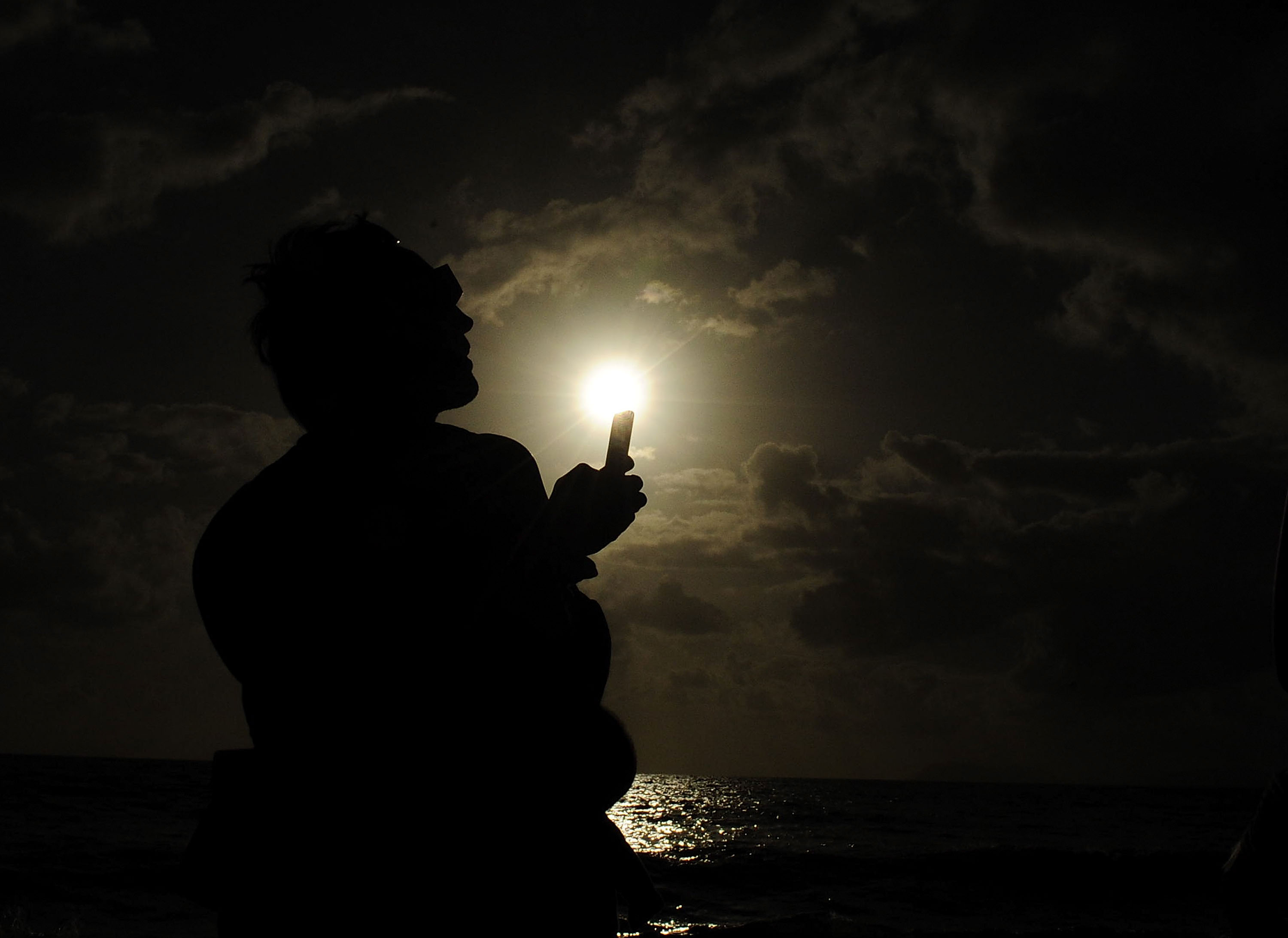 A spectator attempts to take a picture with his phone during the solar eclipse on Wednesday in Palm Cove, Australia. Thousands of eclipse-watchers have gathered in part of North Queensland to enjoy the solar eclipse, the first in Australia in a decade.