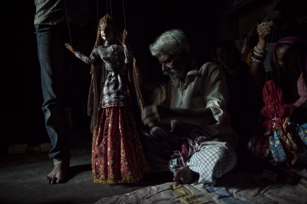 One-Eyed Bhatt is one of the few remaining master puppeteers. Here he readies one of his puppets for performance, unraveling some of the 18 strings that are used to bring the figures to life. One-Eyed Bhatt is the oldest puppeteer remaining in Kathputli. He spent his childhood as an itinerant performer, playing music, puppeteering and telling mythic tales in small villages.