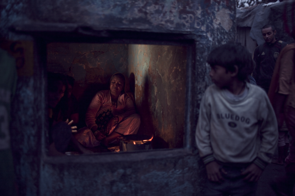 A mother warming a fire for the evening meal.