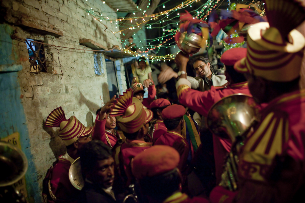 A wedding band gathers around the entrance of the groom's house in one of the colony's many celebrations. During the run-up to the event, the streets flood with people; rupees are tossed in the air; and drum processions compete with one another for speed and intensity.
