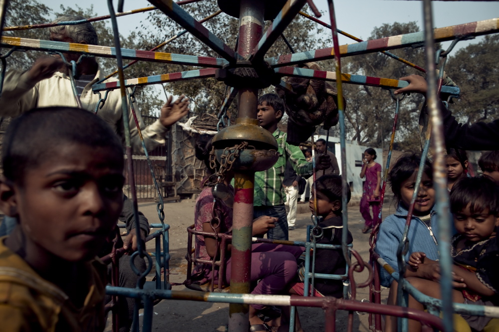 Young children gather on a spinner as an old man turns the wheel.