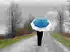 Person with umbrella walking on rainy country road.