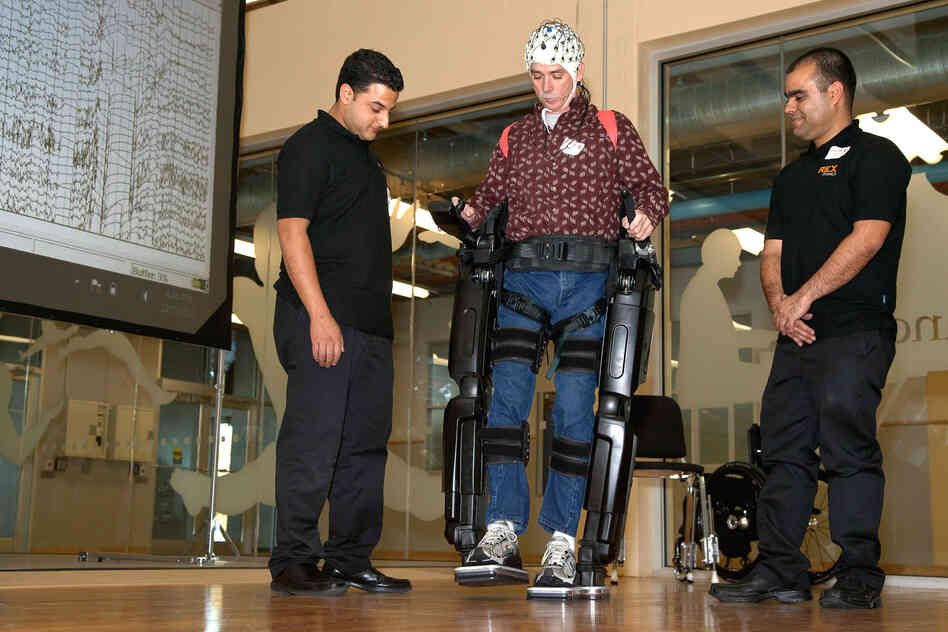 Steve Holbert (center), a paraplegic, demonstrates NeuroRex, a bionic exoskeleton suit augmented with a neural interface cap, developed by researchers at the University of Houston. Holbert controlled the robot's movements with his thoughts.