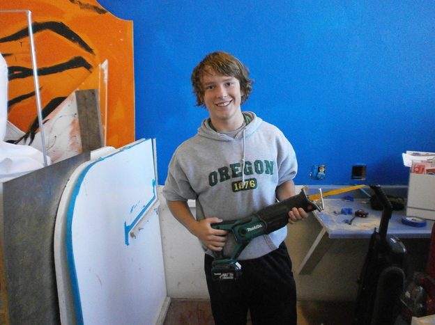 Austin Hay holds a reciprocating saw, which he used to cut part of an existing counter in the workshop so students could build storage space.