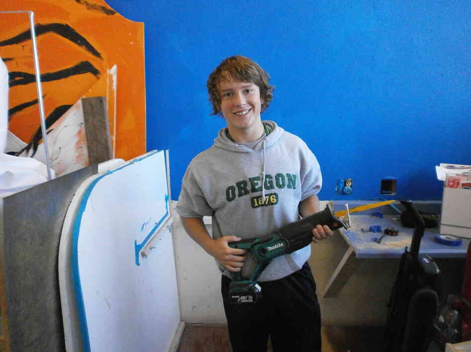 Austin Hay holds a reciprocating saw, which he used to cut part of an existing counter in the workshop so students could build storage space.