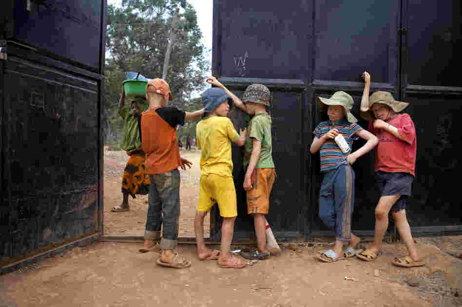 Boys hang out by the gate guarding the Kabanga Protectorate Center, as a local village girl walks by outside, in Kabanga, Tanzania.